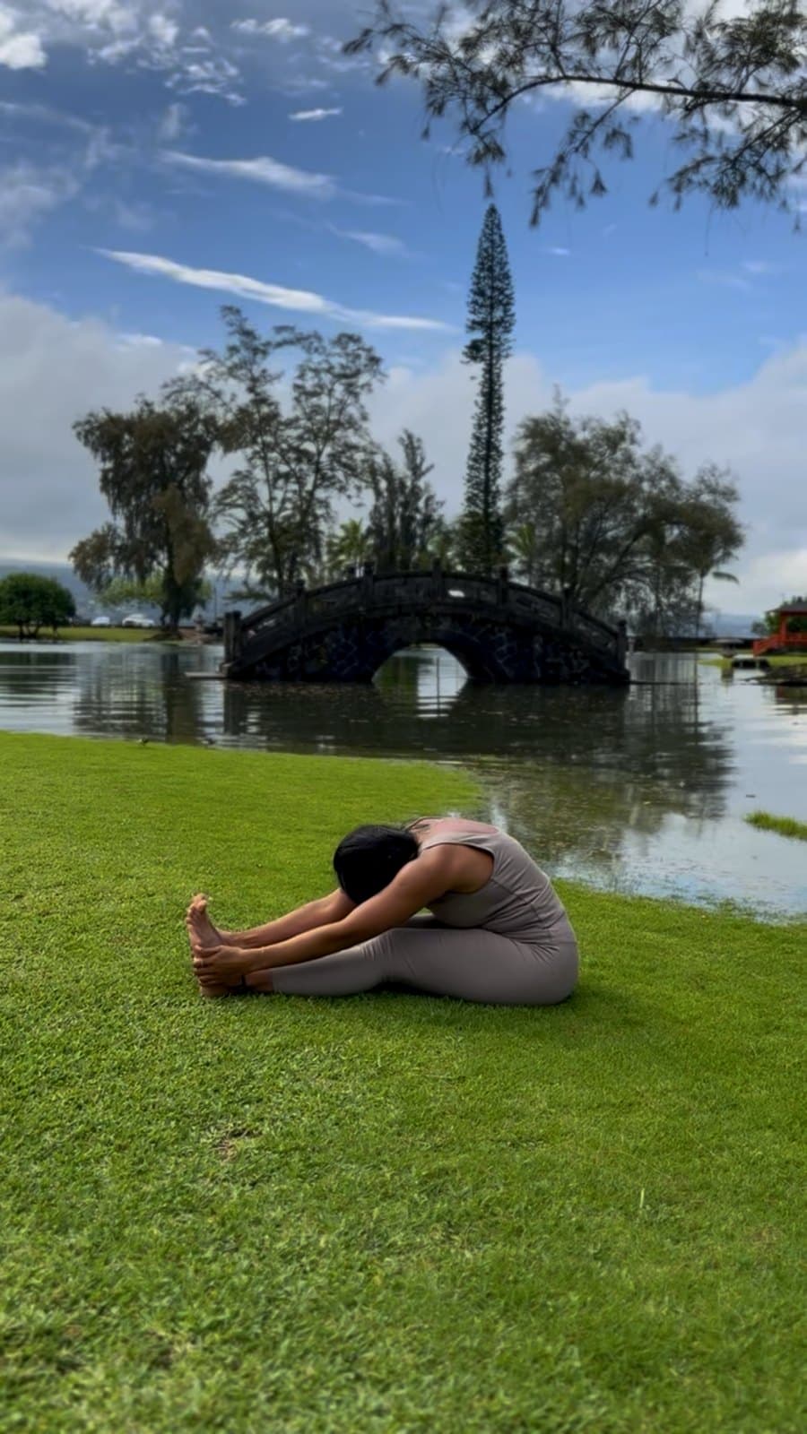 Seated forward fold on the grass beside a stone bridge.